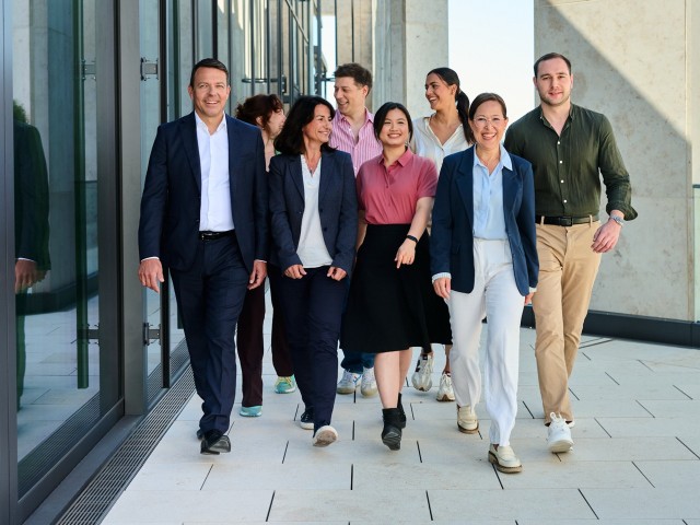 A group of laughing people walking alongside a glass-fronted building.