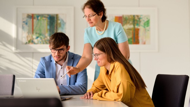 Zwei Frauen und ein Mann vor an einem Tisch vor einem geöffneten Laptop. 