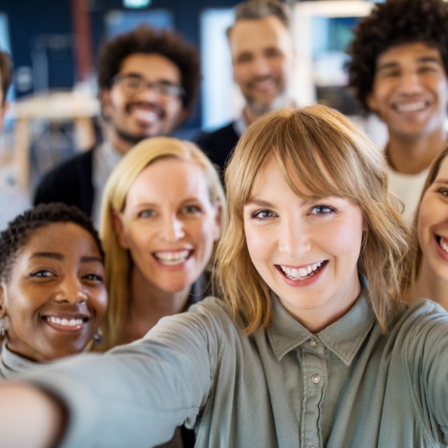 Ein Selfie von vier Frauen im Vordergrund und vier verschwommenen Männern im Hintergrund.
