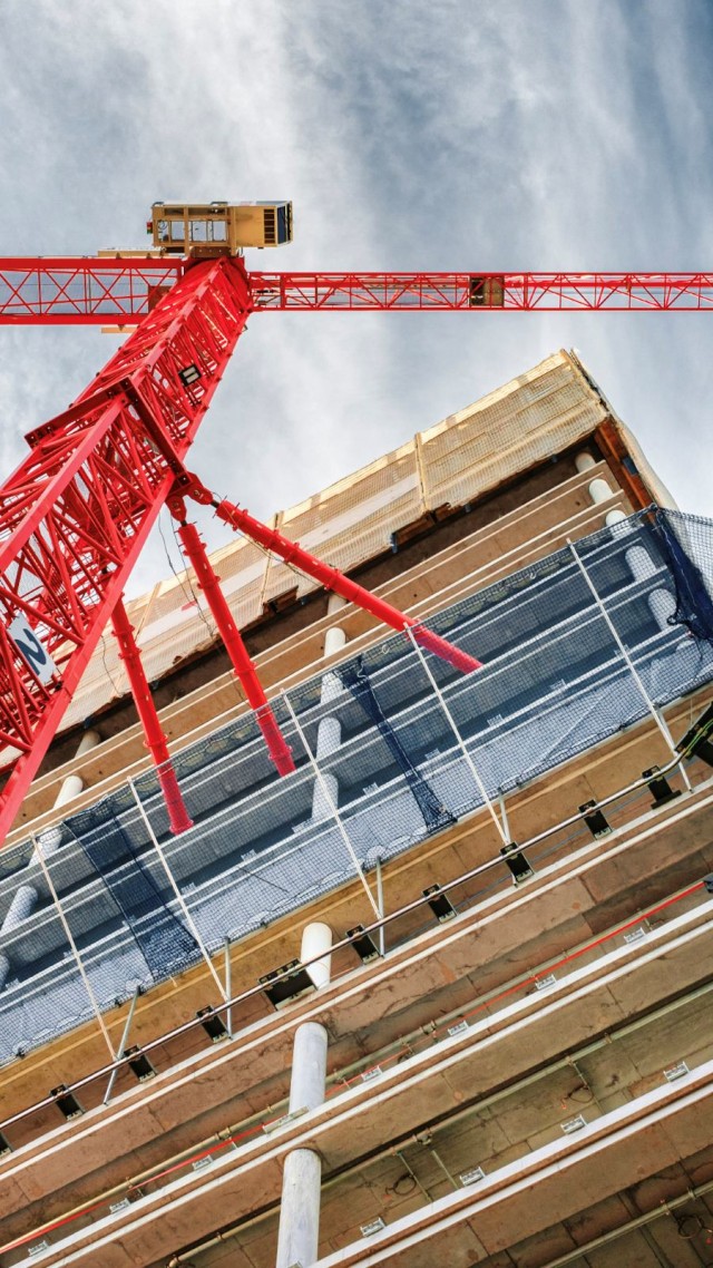 A red crane from a worm’s-eye view, attached to the shell of a building with three red pipes.